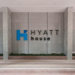 Entrance of Hyatt House Kuala Lumpur, Mont Kiara featuring a large logo on a stone wall, bordered by pillars and green plants.